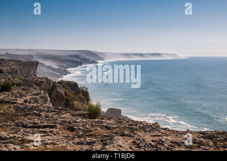 Vista dal bordo di una scogliera su altre falesie, parzialmente nascosti in una nebbia durante una marea alta. Blu cielo di autunno. Orizzonte dell'Oceano Atlantico. Foto Stock