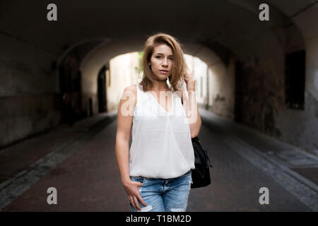 Ritratto di posa bella giovane donna, con in mano i suoi capelli corti. Ombra in un tunnel come un interessante sullo sfondo. Foto Stock