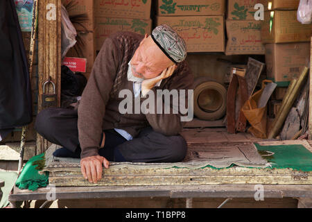 Il vecchio negoziante di uighur si addormentò di fronte al suo negozio, la città vecchia di Kashgar, la regione autonoma di Xinjiang, la Cina. Foto Stock