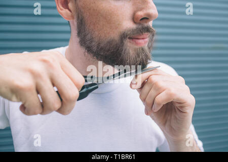 Vista di taglio del barbuto uomo con le forbici in mano e pezzo di barba in un'altra. Il ragazzo è andando a tagliare alcuni peli. Egli guarda fiducioso e calma. Foto Stock