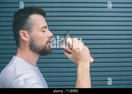 Adulto è in posizione eretta e pronto a bere la bevanda calda da thermos. Egli ha chiuso i suoi occhi. Isolato su striped e sfondo blu. Foto Stock