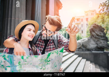 Barbuto giovane uomo stand con la donna e guardare a lei. Egli punti in avanti. Lei tiene la fotocamera e guardare in alto. Turista femminile sorrisi. Egli tiene in mano il suo Foto Stock