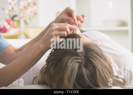 Terapista di agopuntura applicando aghi di agopuntura per la sua testa della cliente Foto Stock