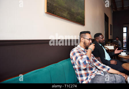 Due uomini con caffè con gli amici in un bar alla moda Foto Stock