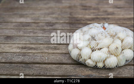 Agricoltura,coltivazione, agricoltura e verdure concetto: cipolla bianca piccola in una pezza di rete di plastica Sacchi,preparati per la semina su un tavolo di legno. Foto Stock