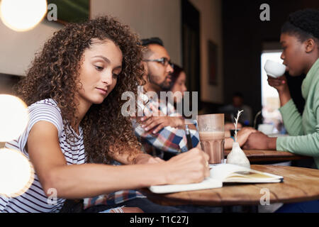 Giovane donna seduta in un bar a scrivere note Foto Stock