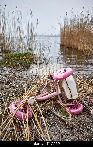 Vecchi rosa triciclo per bambini gettati in una banca di fiume, l'inquinamento ambientale o un concetto di criminalità immagine. Foto Stock