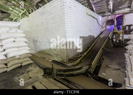 Impianto di tema di magazzino di stoccaggio. Un sacco di tessuto bianco sacchi con prodotti sfusi accatastati in pile al chiuso in produzione. Angar per memorizzare la finitura Foto Stock