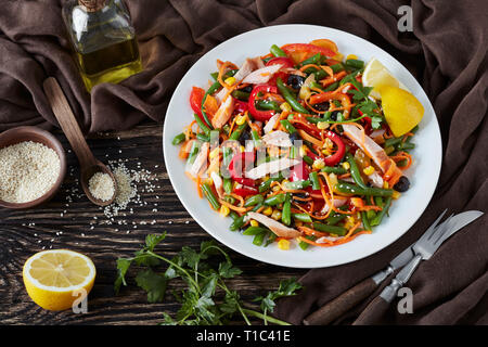 In stile messicano sani con insalata verde fagiolo, peperoni, olive nere, carota, mais e prosciutto tagliato in strisce su una piastra bianca su un tavolo rustico con il da Foto Stock