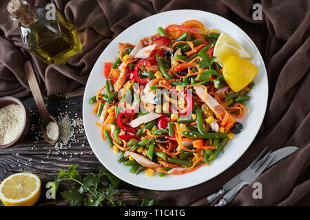 Insalata messicana con verde fagiolo, peperoni, olive nere, carota, mais e prosciutto tagliato in strisce su una piastra bianca su un tavolo rustico con il marrone scuro stoffa Foto Stock