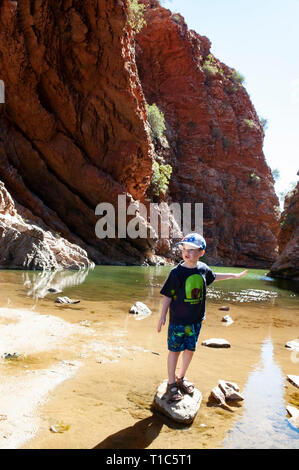 Un 6 anno vecchio ragazzo gioca sulle pietre miliari nelle acque basse di The Simpsons Gap, Territorio del Nord, l'Australia Foto Stock