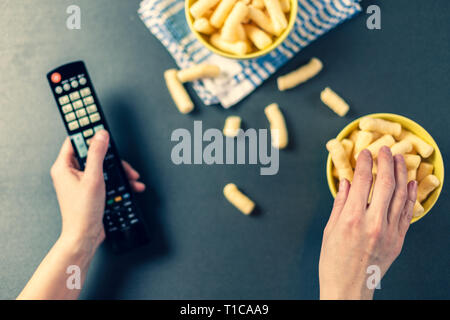 Persona con il telecomando della TV guardare la tv e mangiare patatine , vista superiore Foto Stock