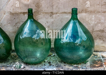 Due enormi vetro verde vuoto giare di vino posto in una fila che riflette la straordinaria architettura di Matera, Basilicata, Italia e moody nuvoloso somma Foto Stock