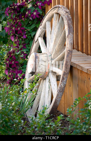 Vecchia ruota di carro contro la recinzione in giardino di fiori per decorazione paesaggistica Foto Stock