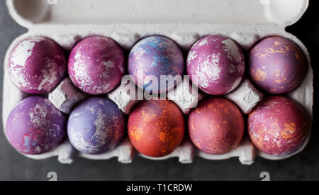 Colorate le uova di pasqua in una scatola di cartone su sfondo scuro. Concetto di sfondo di Pasqua Foto Stock