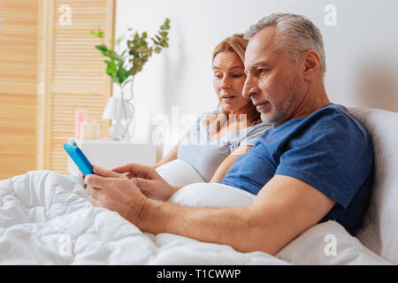 Grey-haired marito mostra morning news su tablet a sua moglie Foto Stock