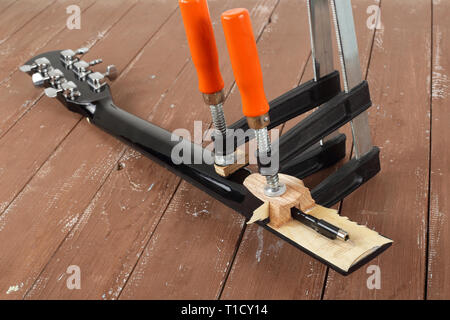 La riparazione di una chitarra e il servizio di assistenza - il serraggio di una chitarra collo sfondo di legno Foto Stock