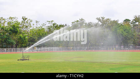 Vecchia macchina di irrigazione, prato erba al campo di calcio, soccer stadium, grandi spray sprinkler corrente a getto di acqua di grandi dimensioni la spruzzatura di sprinkler stre forte Foto Stock