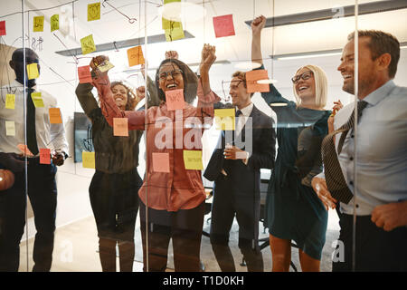 Il tifo gruppo di entusiasti imprenditori saltando su e giù mentre si celebra dopo una sessione di brainstorming con Sticky Notes in un ufficio Foto Stock