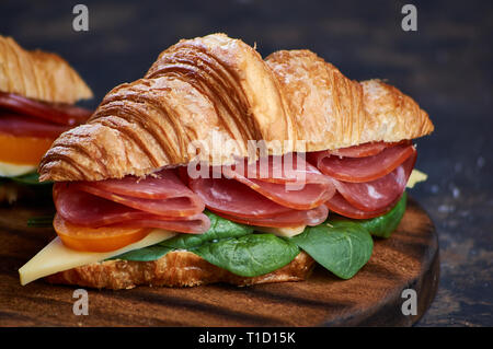 Prosciutto e formaggio sandwich tostato su pane tostato su uno sfondo di legno con carta craft, fresca verdura matura Foto Stock