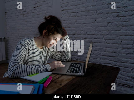 Close up ritratto in luce moody di felice casual donna bella lavorano e studiano su laptop seduto sulla scrivania di notte. Nel lavorare da casa, online Foto Stock