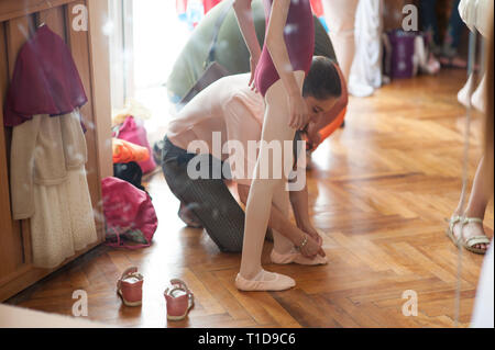 Giovane madre lacci delle scarpe di legatura sulla sua figlia palestra scarpe durante il concerto di danza preparazione Foto Stock