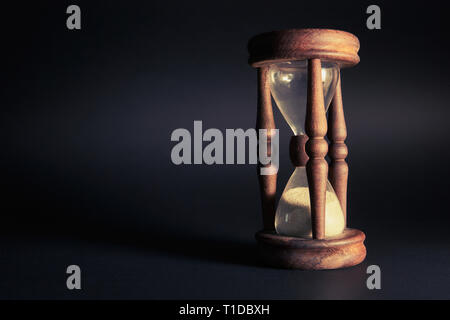 Orologio di sabbia su uno sfondo nero con lunghe ombre Foto Stock