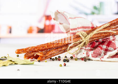 Sacco di tutto il salame piccante stick tyrolini legato da iuta con pepe nero in una cucina bianca Foto Stock