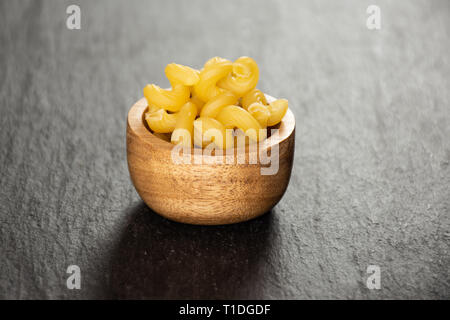 Sacco di tutta la pasta cavatappi con ciotola di legno su pietra grigia Foto Stock