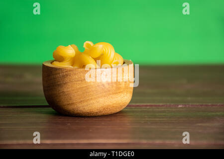 Sacco di tutta la pasta cavatappi con ciotola di legno con schermo verde dietro Foto Stock