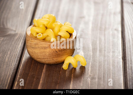 Sacco di tutta la pasta cavatappi con ciotola di legno su legno marrone Foto Stock