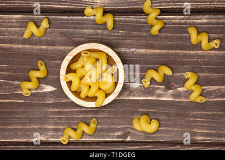 Sacco di tutta la pasta cavatappi con ciotola di legno flatlay su legno marrone Foto Stock