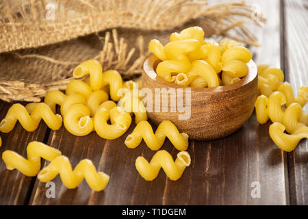 Sacco di tutta la pasta cavatappi con ciotola di legno in un sacco di iuta su legno marrone Foto Stock