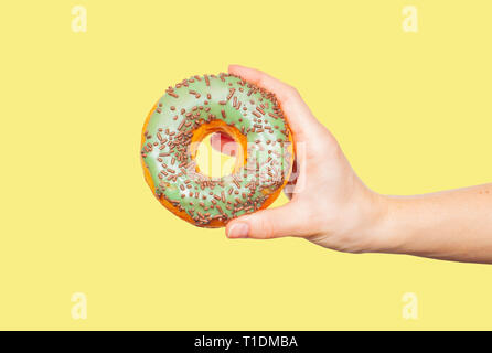 Femmina di mano azienda ciambella. Ciambella colorati pastello su sfondo giallo Foto Stock