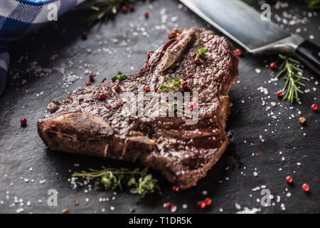 Carni bovine T-bone steak con sale pepe e rosmarino sulla piastra di ardesia. Foto Stock