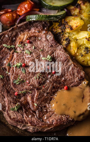 Succosa carne di manzo Costata di manzo patate arrosto con salsa di verdure grigliate sale pepe e le erbe aromatiche in padella vintage. Foto Stock