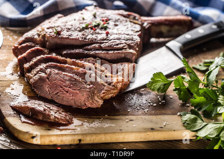 Grigliata di fresco bistecca tomahawk sulla piastra di ardesia con sale e pepe e rosmarino prezzemolo erbe aromatiche. Fette di pezzi di succosa bistecca di manzo Foto Stock