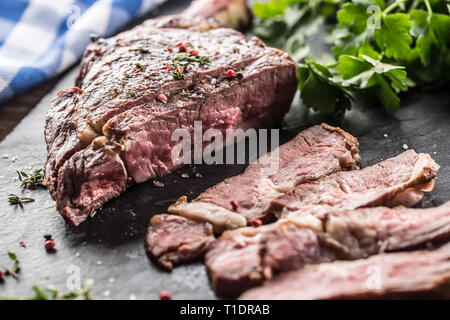 Grigliata di fresco bistecca tomahawk sulla piastra di ardesia con sale e pepe e rosmarino prezzemolo erbe aromatiche. Fette di pezzi di succosa bistecca di manzo Foto Stock