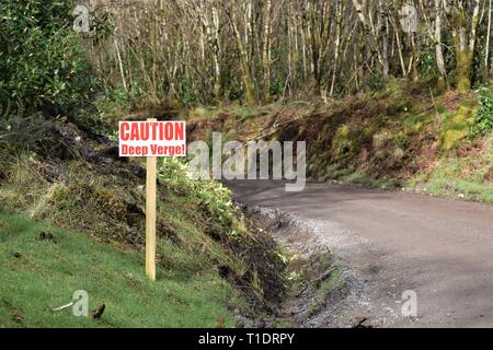 Attenzione segno da parte di orlo fosso di una nuova strada sterrata curva a sinistra con piccoli tronchi di alberi in background. Foto Stock