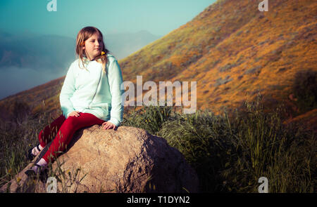 Una ragazza si siede su una roccia tra i fiori selvaggi super bloom nel lago Elsinore, California primavera 2019 Foto Stock