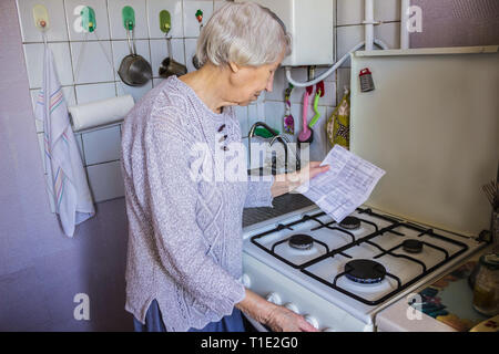 Senior vecchia massaia a casa ed esamina il gas e elettricità Foto Stock