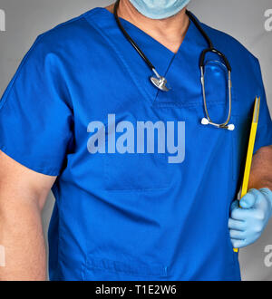 Dottore in uniforme blu e sterili Guanti di lattice, uno stetoscopio è appeso sul suo collo e sfondo grigio Foto Stock