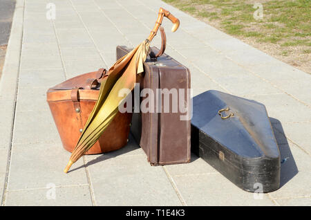 Vintage elementi di bagaglio, valigia, ombrello, hat box e strumento musicale in piedi su un marciapiede in presenza di luce solare. Foto Stock