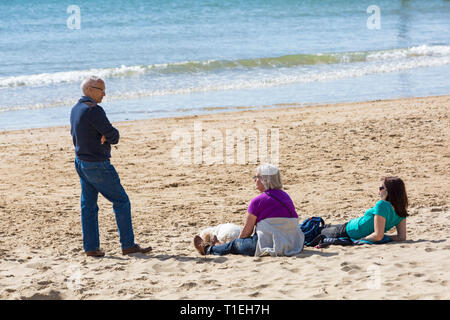 Bournemouth Dorset, Regno Unito. 26 Mar, 2019. Regno Unito meteo: un altro bel giorno caldo e soleggiato con un cielo azzurro e il sole caldo a Bournemouth spiagge, come i visitatori in testa al mare per rendere la maggior parte del tempo splendido. Uomo maturo in piedi a chiacchierare con due donne sedute sulla sabbia. Credito: Carolyn Jenkins/Alamy Live News Foto Stock