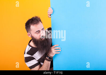 Ritratto di uomo barbuto bloccata la sua testa fuori dietro un pannello di blu su sfondo giallo. Uomo bello. Foto Stock
