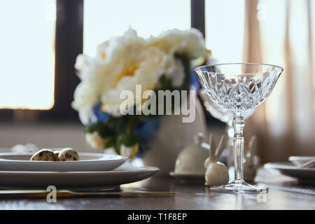 Messa a fuoco selettiva del vetro cristallo, mazzo di fiori in vaso e conigli decorativo su un tavolo di legno a casa Foto Stock