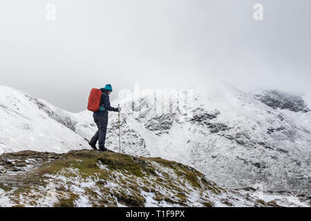 Walker sul Vertice di Outerside con montagne coperte di neve di vela al di là, Lake District, Cumbria, Regno Unito Foto Stock