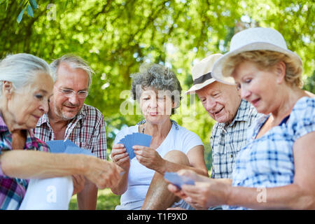 Senior amici giocando a carte insieme nel parco in estate come un passatempo Foto Stock