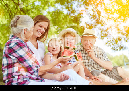 Estesa famiglia con bambino di mangiare il melone in estate in giardino Foto Stock