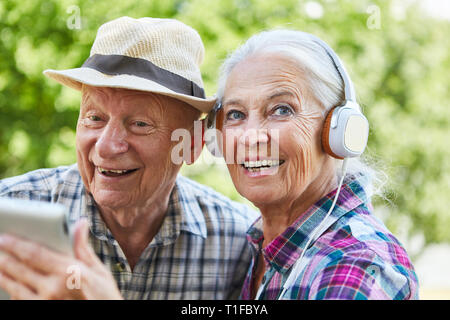 Coppia di anziani con cuffie e computer tablet ascolta musica in natura in estate Foto Stock